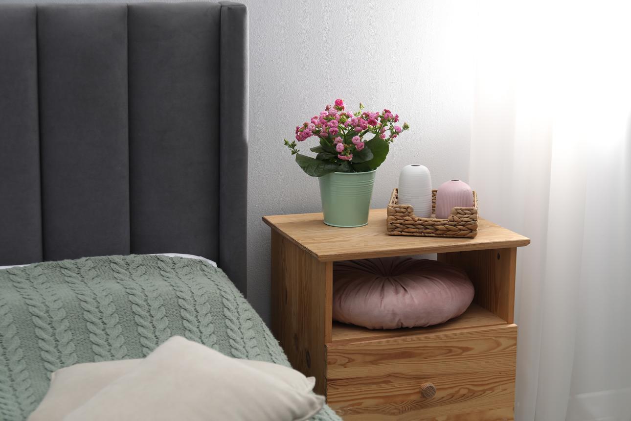 Bedside table with flowers and decor near bed indoors